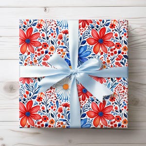 Puede incluir: Un regalo envuelto con papel de regalo con estampado floral. El papel presenta flores rojas, azules y naranjas sobre un fondo blanco. Una cinta y un lazo de satén azul claro están atados alrededor del regalo.