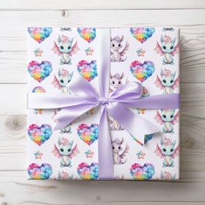 May include: A wrapped gift with white wrapping paper featuring a repeating pattern of pastel dragons, rainbow hearts, and stars. A lavender satin ribbon and bow secure the package, creating a whimsical and colorful presentation.