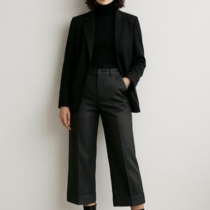 Pode incluir: Uma pessoa vestindo um blazer preto, uma gola alta preta e cal&ccedil;as cinza escuro com bainhas dobradas. Ela tamb&eacute;m est&aacute; usando botas de tornozelo pretas. A roupa &eacute; de estilo moderno e minimalista.