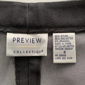 Pode incluir: Close-up de um par de cal&ccedil;as cinza escuro. A etiqueta diz "PREVIEW COLLECTION" e lista a composi&ccedil;&atilde;o do tecido: 53% nylon, 43% poli&eacute;ster e 4% spandex. O tamanho &eacute; 8.