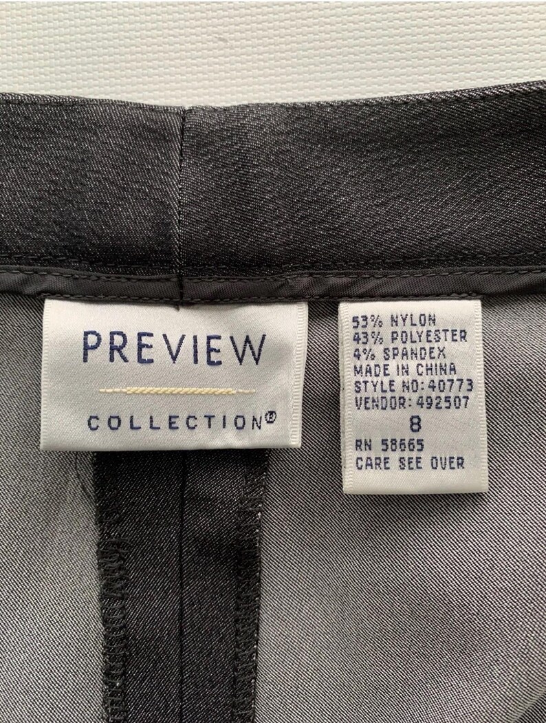 Pode incluir: Close-up de um par de cal&ccedil;as cinza escuro. A etiqueta diz "PREVIEW COLLECTION" e lista a composi&ccedil;&atilde;o do tecido: 53% nylon, 43% poli&eacute;ster e 4% spandex. O tamanho &eacute; 8.