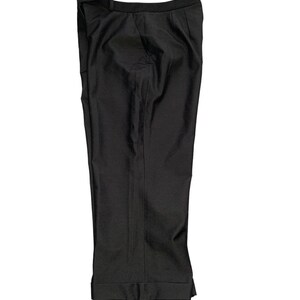 Pode incluir: Cal&ccedil;as pretas de fato com bainha dobrada. As cal&ccedil;as t&ecirc;m um design cl&aacute;ssico com perna reta e corte sob medida. O tecido parece ser um material preto liso e uniforme. As cal&ccedil;as est&atilde;o dobradas ao meio.