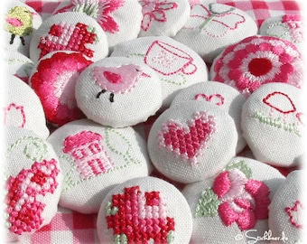May include: A collection of 15 white fabric buttons with various embroidered designs in pink and green. The designs include a bird, a house, a heart, a flower, and a cup.