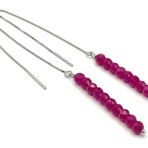 Op de afbeelding: Een paar zilveren oorhangers met een lange ketting en een rij roze facetgeslepen kralen.