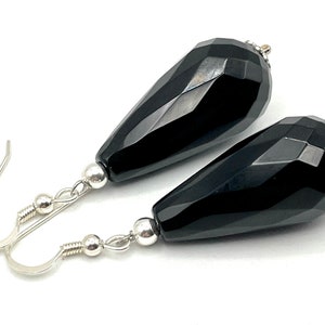 May include: A pair of black onyx teardrop earrings with silver hooks and beads. The earrings are faceted and have a high polish.