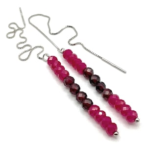 May include: A pair of threader earrings featuring silver-tone box chains attached to vertical rows of faceted beads. The beads transition in colour from bright fuchsia at the top, to deep dark red in the centre, and back to bright fuchsia at the base.