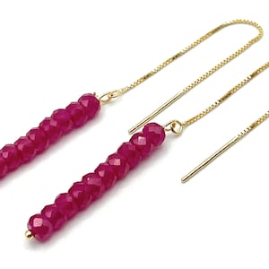 May include: A pair of pink gemstone dangle earrings with gold chains. The earrings are made of faceted pink gemstones and gold chains.