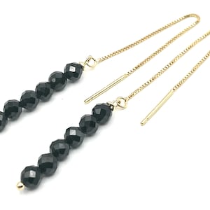 以下が含まれることがあります： 金色のチェーンが付いた、黒い宝石のぶら下がりイヤリングのペア。イヤリングは、黒いファセットカットのビーズの列が特徴です。