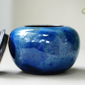 K&ouml;nnte beinhalten: Eine blaue Keramikdose mit Deckel. Die Dose hat eine gefleckte blaue und wei&szlig;e Glasur mit gl&auml;nzender Oberfl&auml;che. Der Deckel ist dunkelbraun.