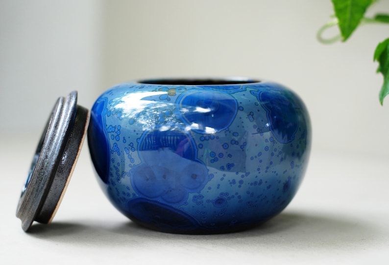 K&ouml;nnte beinhalten: Eine blaue Keramikdose mit Deckel. Die Dose hat eine gefleckte blaue und wei&szlig;e Glasur mit gl&auml;nzender Oberfl&auml;che. Der Deckel ist dunkelbraun.