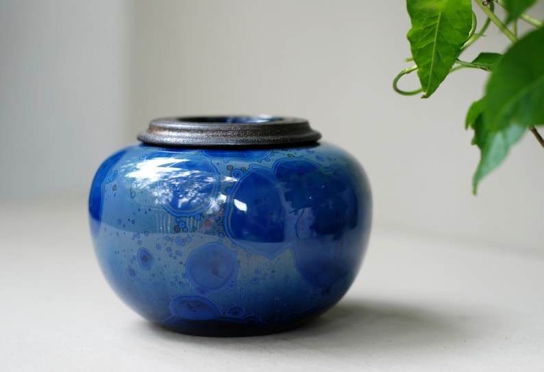 K&ouml;nnte beinhalten: Eine blaue Keramikdose mit einem dunkelbraunen Deckel. Die Dose hat ein marmoriertes Muster mit blauen und wei&szlig;en Wirbeln.
