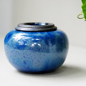 K&ouml;nnte beinhalten: Eine blaue Keramikdose mit einem dunkelgrauen Deckel. Die Dose hat eine gesprenkelte Glasur mit einem wirbelnden Muster.