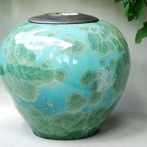 Può includere: Un grande vaso rotondo in ceramica con una smaltatura verde e blu. Il vaso ha un coperchio in legno.