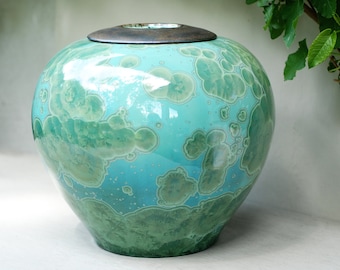 Könnte beinhalten: Eine große, runde Keramikvase mit einer grün-blauen Glasur. Die Vase hat einen Holzdeckel.
