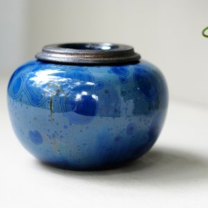 K&ouml;nnte beinhalten: Eine kleine, runde, blaue Keramikdose mit einem silbernen Deckel. Die Dose hat ein gesprenkeltes, marmoriertes Design.