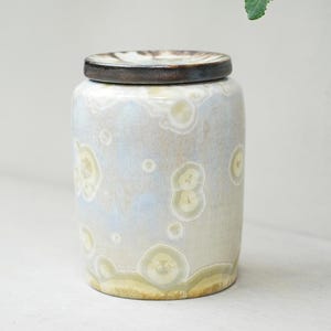 Pode incluir: Um pote de cerâmica com tampa, com um esmalte salpicado azul claro e branco. O pote tem uma forma redonda e uma boca larga.