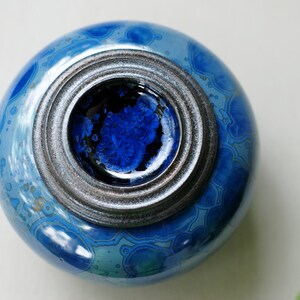 K&ouml;nnte beinhalten: Eine blaue Keramikdose mit einem silbernen Deckel. Die Dose hat ein wirbelndes Muster und ein blaues und schwarzes Inneres.