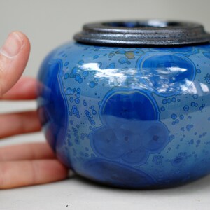 K&ouml;nnte beinhalten: Eine blaue Keramikdose mit Deckel. Die Dose hat eine gefleckte blaue Glasur mit einem Muster aus kleinen wei&szlig;en Blasen.