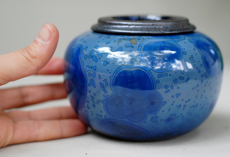 K&ouml;nnte beinhalten: Eine blaue Keramikdose mit Deckel. Die Dose hat eine gefleckte blaue Glasur mit einem Muster aus kleinen wei&szlig;en Blasen.