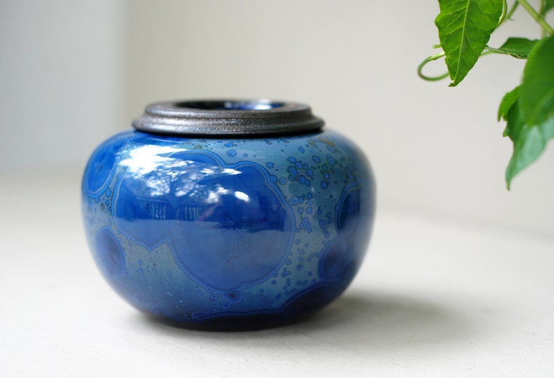 K&ouml;nnte beinhalten: Eine blaue Keramikdose mit einem dunkelgrauen Deckel. Die Dose hat ein wirbelndes Muster aus Blau und Wei&szlig;.