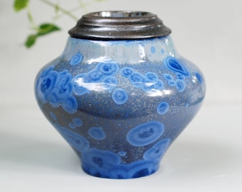 Könnte beinhalten: Eine blaue und graue Keramikurne mit Deckel. Die Urne hat eine gesprenkelte Glasur mit blauen Kreisen.
