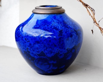 Op de afbeelding: Een blauwe keramische urn met een bruin deksel. De urn heeft een marmereffect met donkerblauwe en witte swirls.