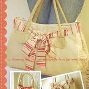 May include: A beige tote bag with a red and white striped ribbon bow. The bag has a brown leather handle and a zipper closure. The bag is made of a canvas material and has a  "Bella" label on the front.