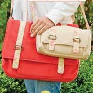 May include: Two canvas school bags with adjustable straps. The larger bag is red with white floral print and the smaller bag is beige with white floral print. Both bags have brown leather buckles.