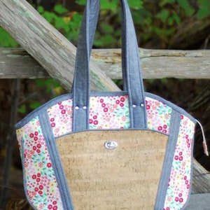 May include: A floral print tote bag with a cork front panel and denim-like accents. The bag features a zipper closure and sturdy handles. The floral pattern includes pink, red, and yellow flowers on a white background.