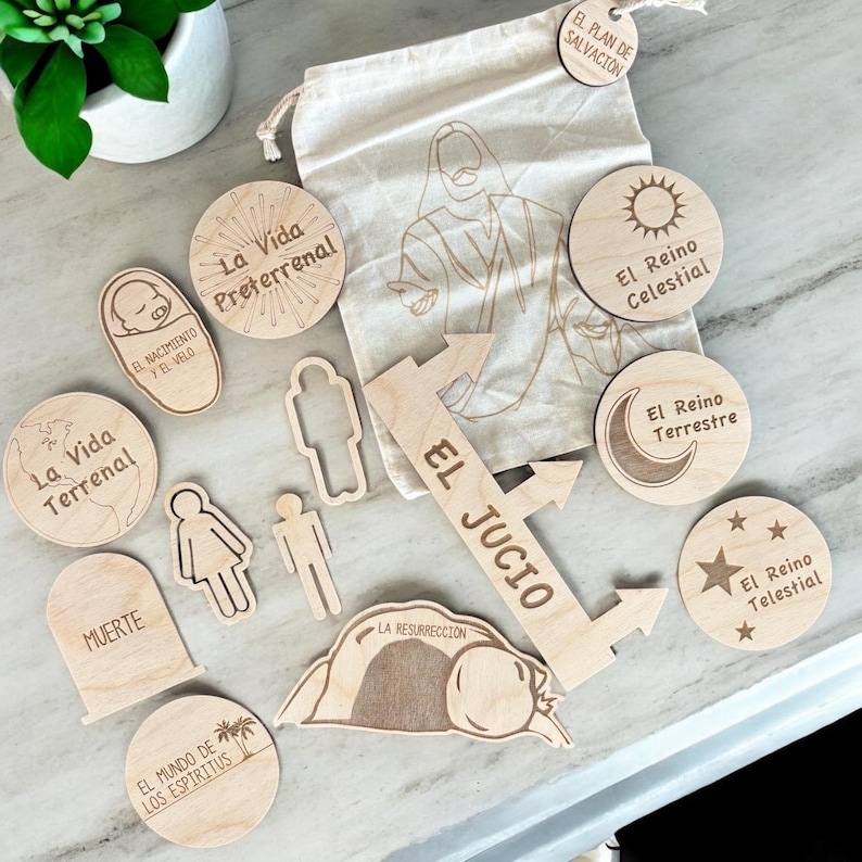 May include: Wooden craft pieces with Spanish text, including "La Vida Terrenal", "El Jucio", and "La Vida Preterrenal". The pieces are arranged on a light wood surface.