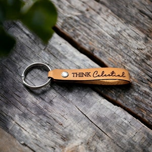 May include: A brown leather keychain with a silver key ring and the text "THINK Celestial" engraved on the leather.