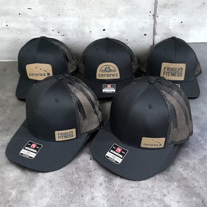 May include: Five black and brown mesh trucker hats with different logos. The logos include "FRUGILO FITNESS", "zerorez", and a mountain range with "zerorez" underneath.