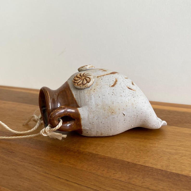 May include: A handmade ceramic hanging planter with a brown and white speckled finish. The planter has a small handle and a decorative spiral design. A natural fiber cord is attached for hanging.