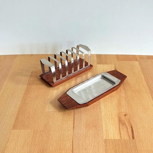 May include: A vintage chrome and wood toast rack with six slots and a matching rectangular tray. The chrome elements are set on a dark wood base. The tray has a stainless steel interior and a dark wood border. The items are displayed on a wooden surface.