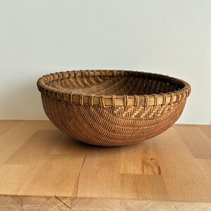 Pu&ograve; includere: Un cesto rotondo e intrecciato di colore marrone naturale. Il cesto ha un design ampio e aperto con un bordo decorativo. &Egrave; realizzato con materiale a trama fitta, creando una superficie strutturata. Il cesto &egrave; appoggiato su una superficie di legno.
