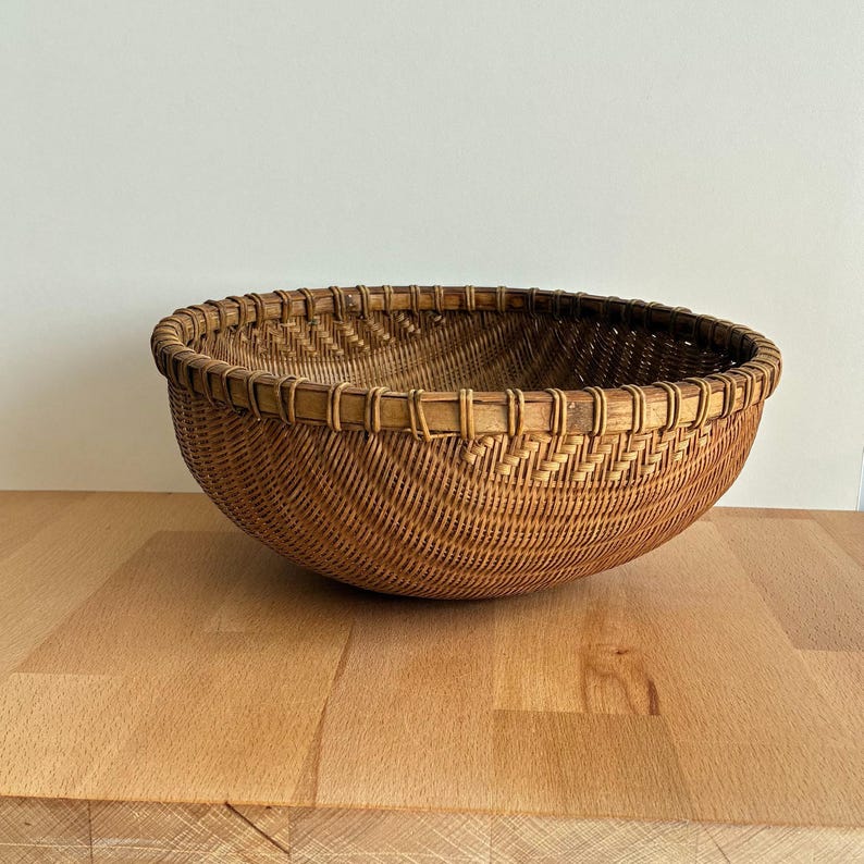 Pu&ograve; includere: Un cesto rotondo e intrecciato di colore marrone naturale. Il cesto ha un design ampio e aperto con un bordo decorativo. &Egrave; realizzato con materiale a trama fitta, creando una superficie strutturata. Il cesto &egrave; appoggiato su una superficie di legno.
