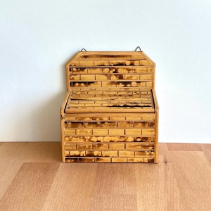 May include: A bamboo recipe box with a hinged lid and a brick-like pattern. The box is made of light brown bamboo with darker brown accents, and has a small metal loop for hanging. The box is sitting on a wooden surface.