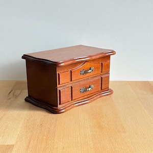 May include: A white ceramic mug with a black handle and the text "But First, Coffee" in a bold, black font. The mug is set against a blurred background, suggesting a cozy setting.