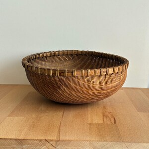 Pu&ograve; includere: Un cesto rotondo intrecciato di colore marrone naturale. Il cesto ha un design ampio e aperto con un motivo decorativo intrecciato sui lati. Il bordo &egrave; rinforzato con una tessitura pi&ugrave; spessa.