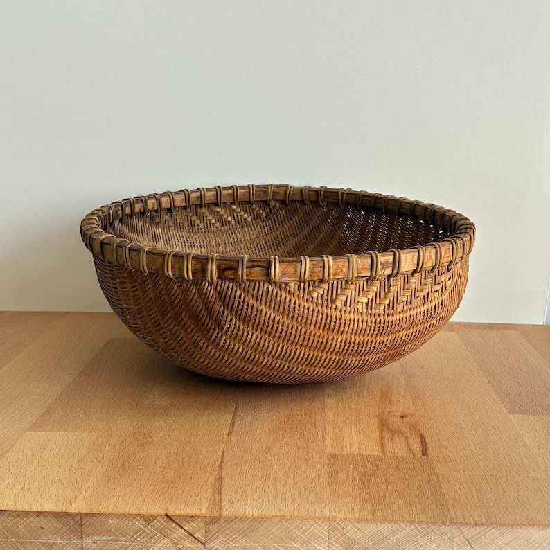 Pu&ograve; includere: Un cesto rotondo intrecciato di colore marrone naturale. Il cesto ha un design ampio e aperto con un motivo decorativo intrecciato sui lati. Il bordo &egrave; rinforzato con una tessitura pi&ugrave; spessa.