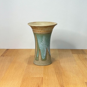 May include: A ceramic vase with a flared rim and a tapered body. The upper portion features a textured tan finish, while the mid-section displays a cascading drip glaze in shades of sage green and white over a speckled, light brown clay base.