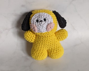 May include: A yellow crocheted plush toy in the shape of a dog with black ears and pink cheeks. The toy has a white face with black eyes and a black nose.