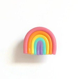 May include: A small, colorful rainbow made of clay. The rainbow is pink, orange, yellow, green, blue, and purple.