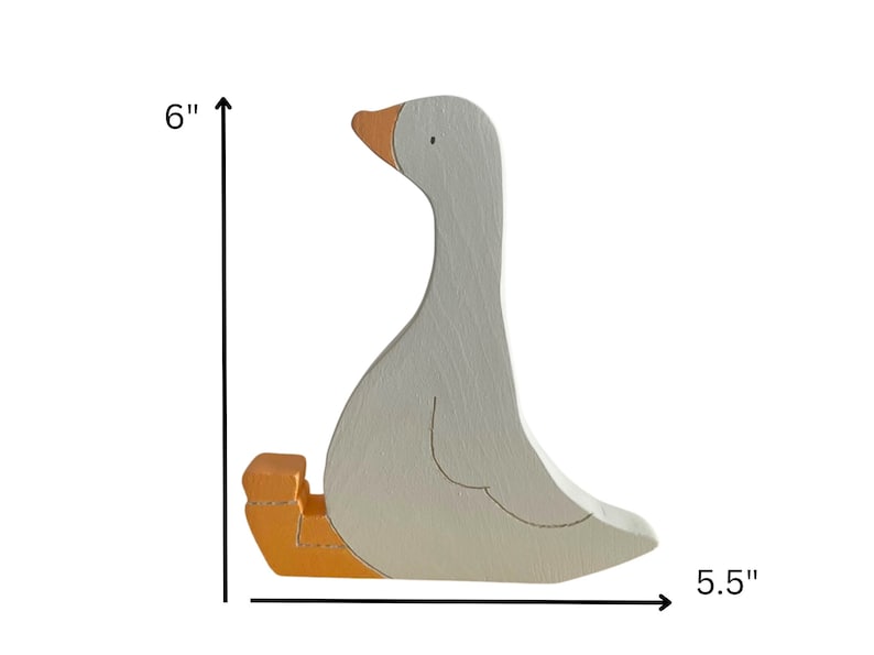May include: A white wooden goose figurine with an orange beak and feet. The goose is sitting down with its head turned to the side. It measures 6 inches tall and 5.5 inches wide.