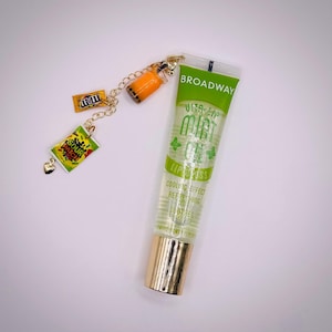 May include: Clear lip gloss tube with a gold cap and green label that reads "Mint Oil Lip Gloss". A charm with a gold chain features miniature candy and a boba tea cup.
