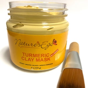 May include: A yellow jar of turmeric clay mask with a wooden applicator brush. The jar has a label that reads "Nature's Ego Turmeric Clay Mask" with the text "Rice Extract" in a smaller font. The label also says "Detoxify, Brighten, Balance, Improve Complexion" and "4 oz (120 g)".