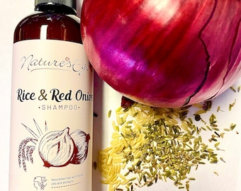 May include: A brown bottle of shampoo with a black pump top. The bottle is labeled "Nature's Ego Rice & Red Onion Shampoo". The bottle is sitting on a white surface with a red onion, rice, and herbs scattered around it.