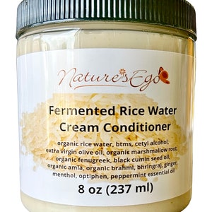 May include: A white plastic jar with a black lid and a label that reads "Nature's Ego Fermented Rice Water Cream Conditioner". The label lists the ingredients, including organic rice water, btms, cetyl alcohol, extra virgin olive oil, organic marshmallow root, organic fenugreek, black cumin seed oil, organic amla, organic brahmi, bhringraj, ginger, menthol, optiphen, and peppermint essential oil. The jar contains 8 ounces (237 ml) of product.