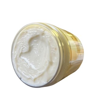 May include: A white jar of body butter with a gold lid. The jar is filled with a thick, creamy product.