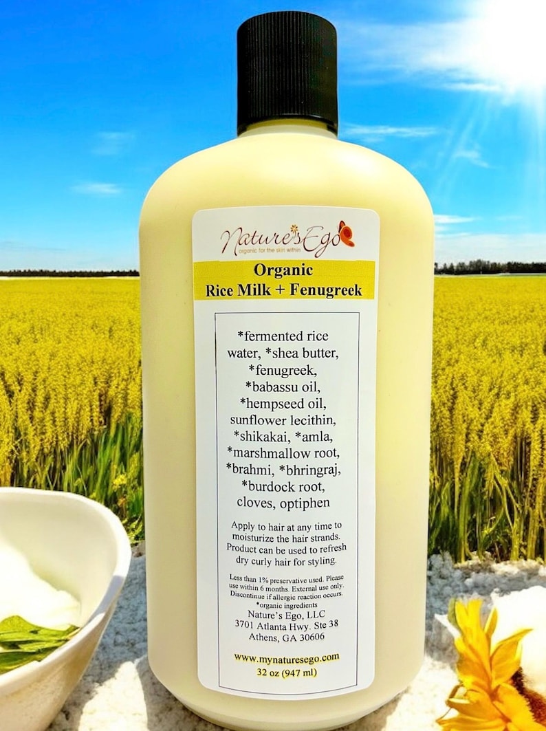 May include: A white plastic bottle with a black cap, labeled "Nature's Ego Organic Rice Milk + Fenugreek". The bottle is in front of a field of yellow flowers. The label lists the ingredients, which include fermented rice water, shea butter, fenugreek, babassu oil, hempseed oil, sunflower lecithin, shikakai, amla, marshmallow root, brahmi, bhringraj, burdock root, cloves, and optiphen. The bottle is 32 ounces (947 ml).